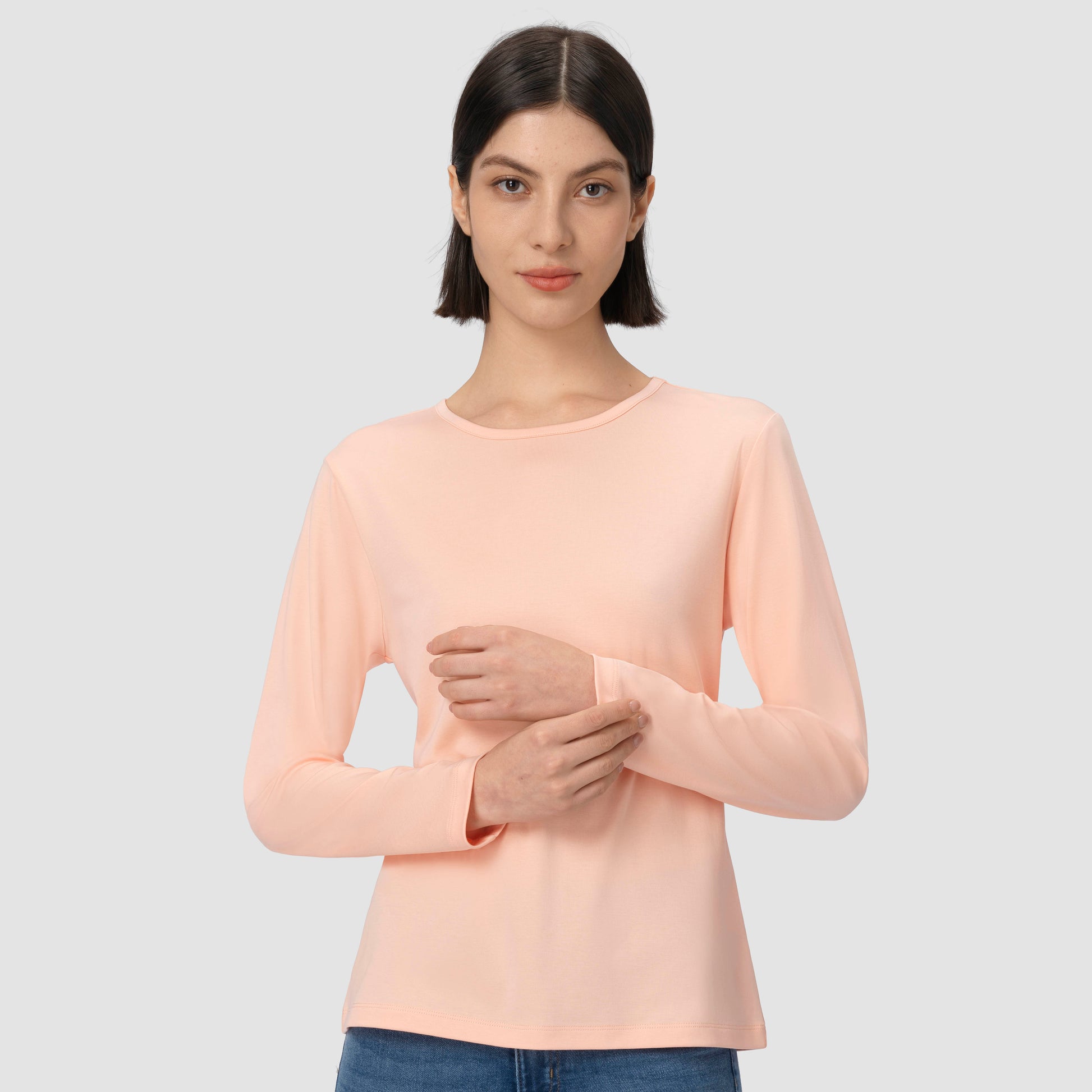 Woman wearing a light pink salmon long-sleeve top on a plain background