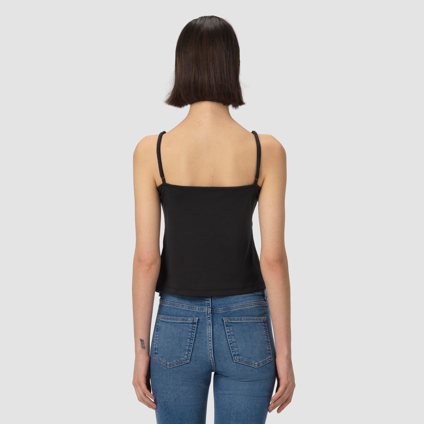 Person wearing a black tank top and blue jeans on a light gray background