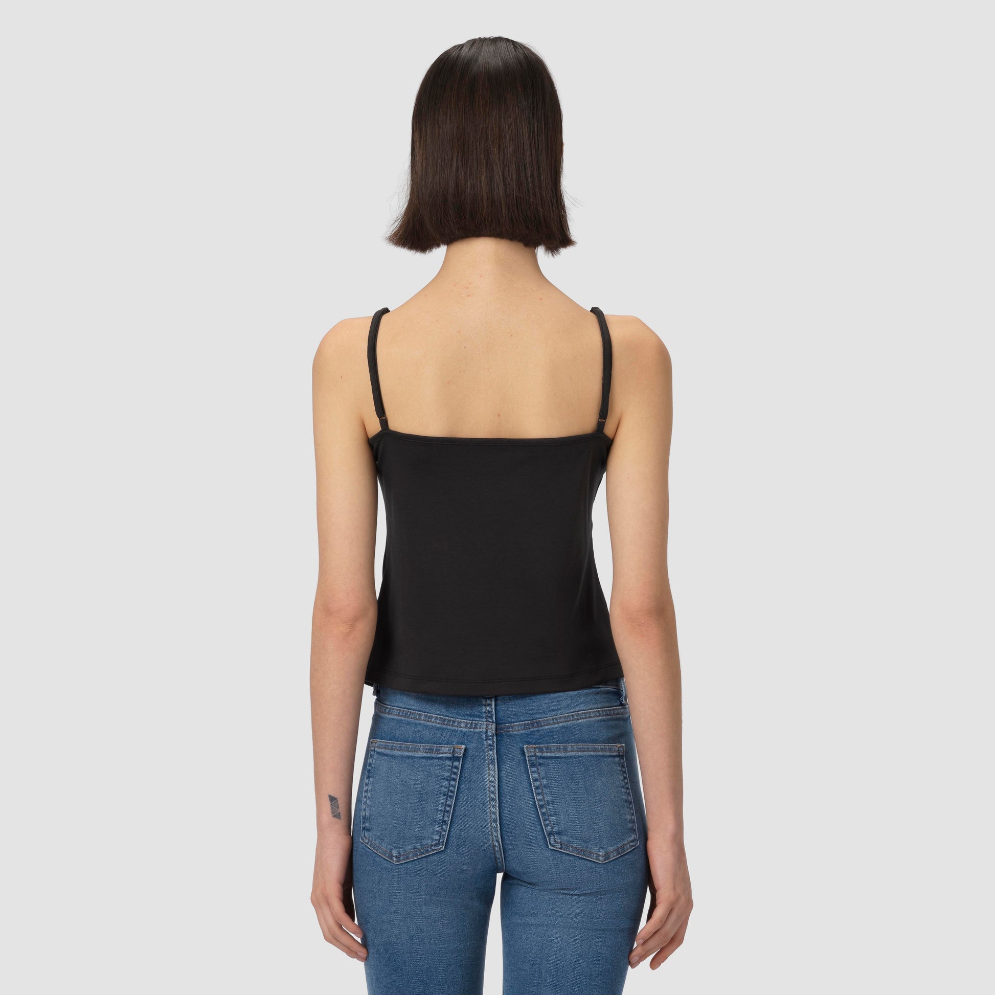 Person wearing a black tank top and blue jeans on a light gray background