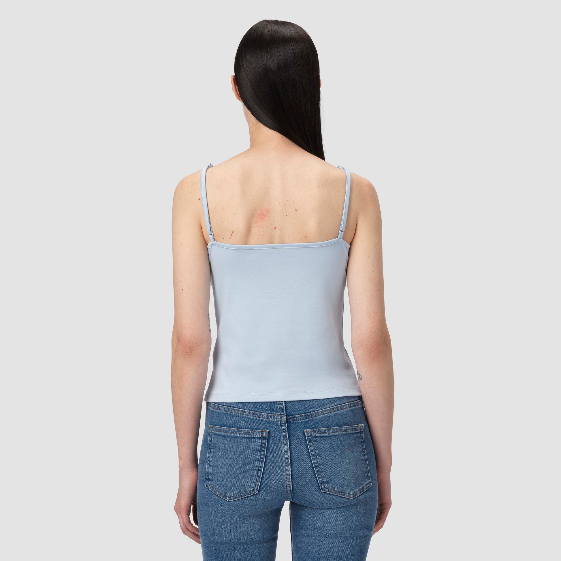 Person wearing a light blue tank top and jeans on a plain background