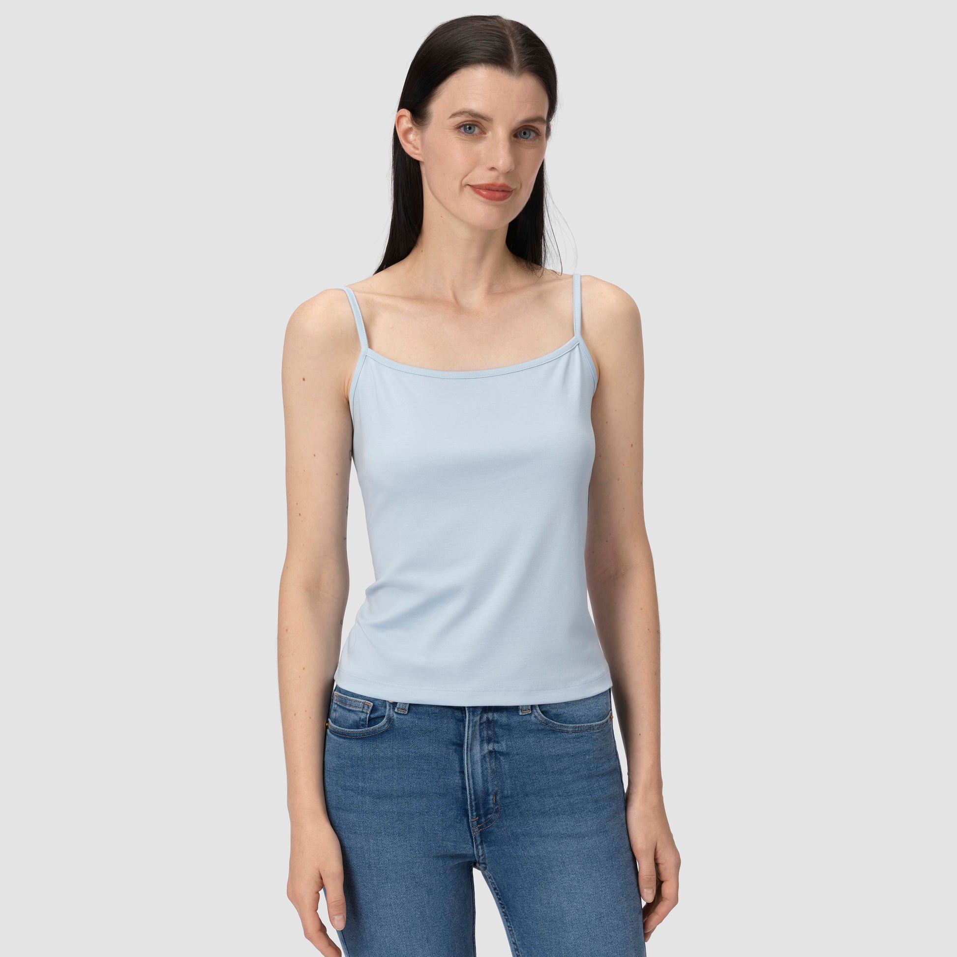 Woman wearing a light blue tank top and blue jeans on a plain background