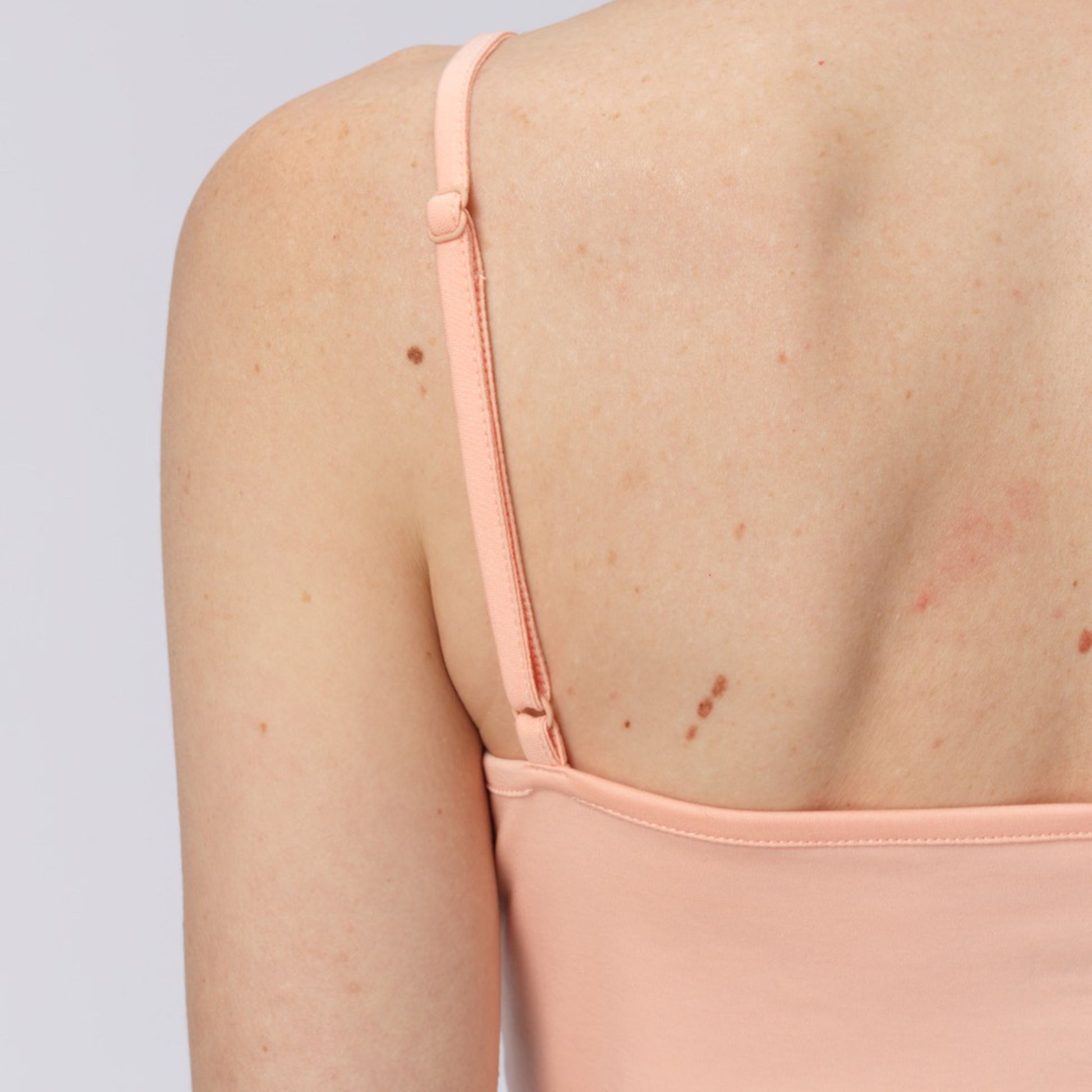 Close-up of a person wearing a light pink salmon long-sleeve top with thin straps on a plain background.