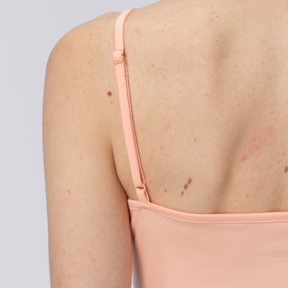 Close-up of a person wearing a light pink salmon long-sleeve top with thin straps on a plain background.