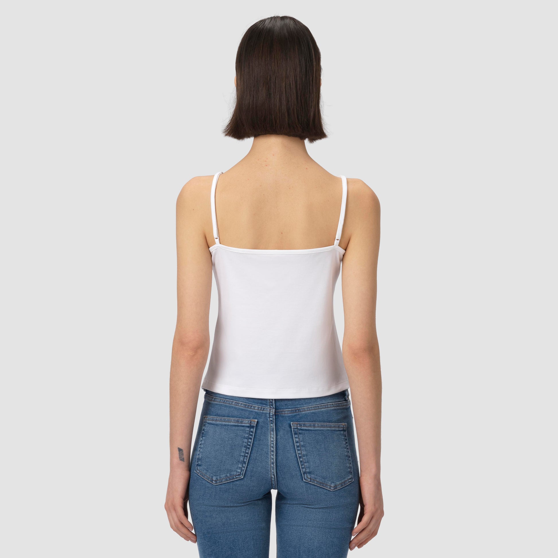Person wearing a white tank top and blue jeans on a plain background