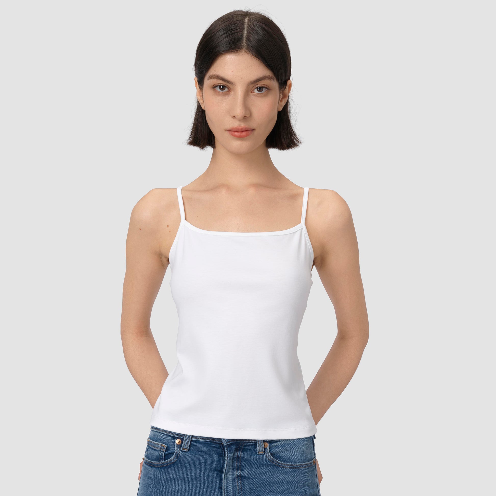 Woman wearing a white tank top and blue jeans against a plain background