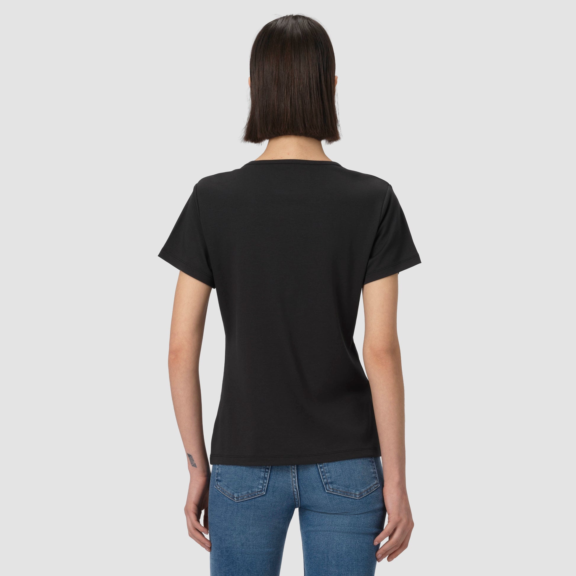 Person wearing a black t-shirt and blue jeans on a light gray background