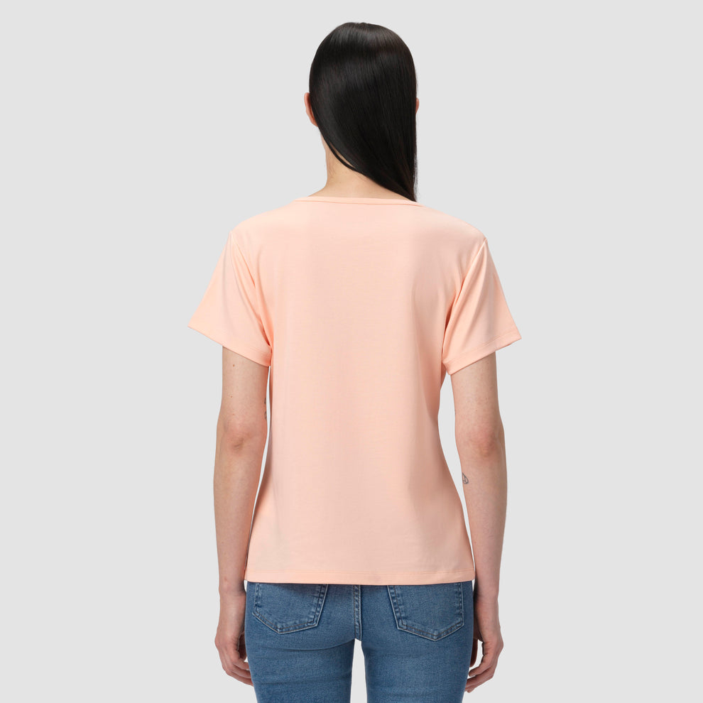 Person wearing a salmon light pink t-shirt and blue jeans on a gray background