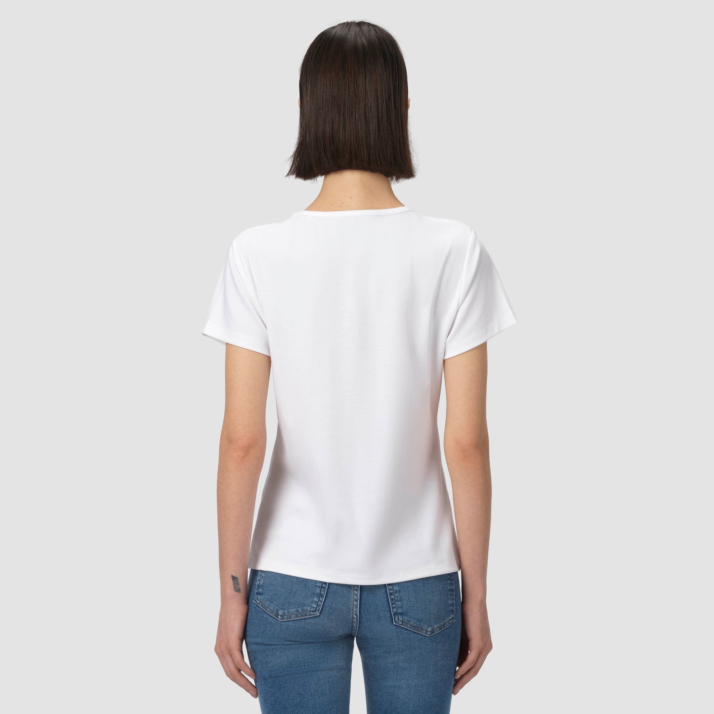 Person wearing a plain white t-shirt and blue jeans on a light gray background