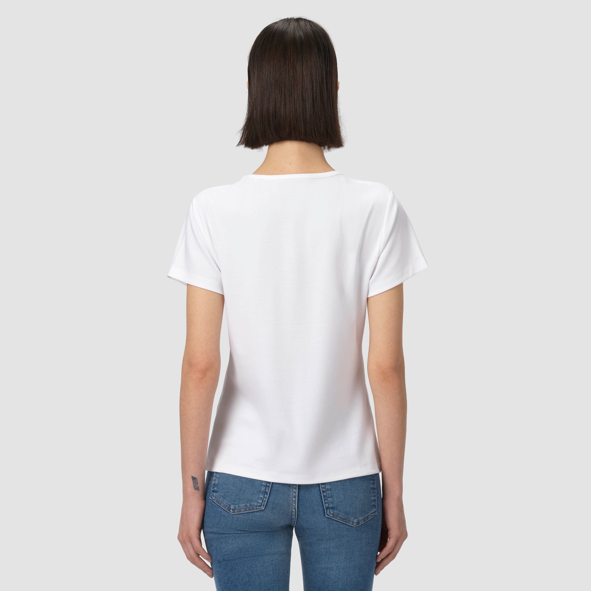 Person wearing a plain white t-shirt and blue jeans on a light gray background