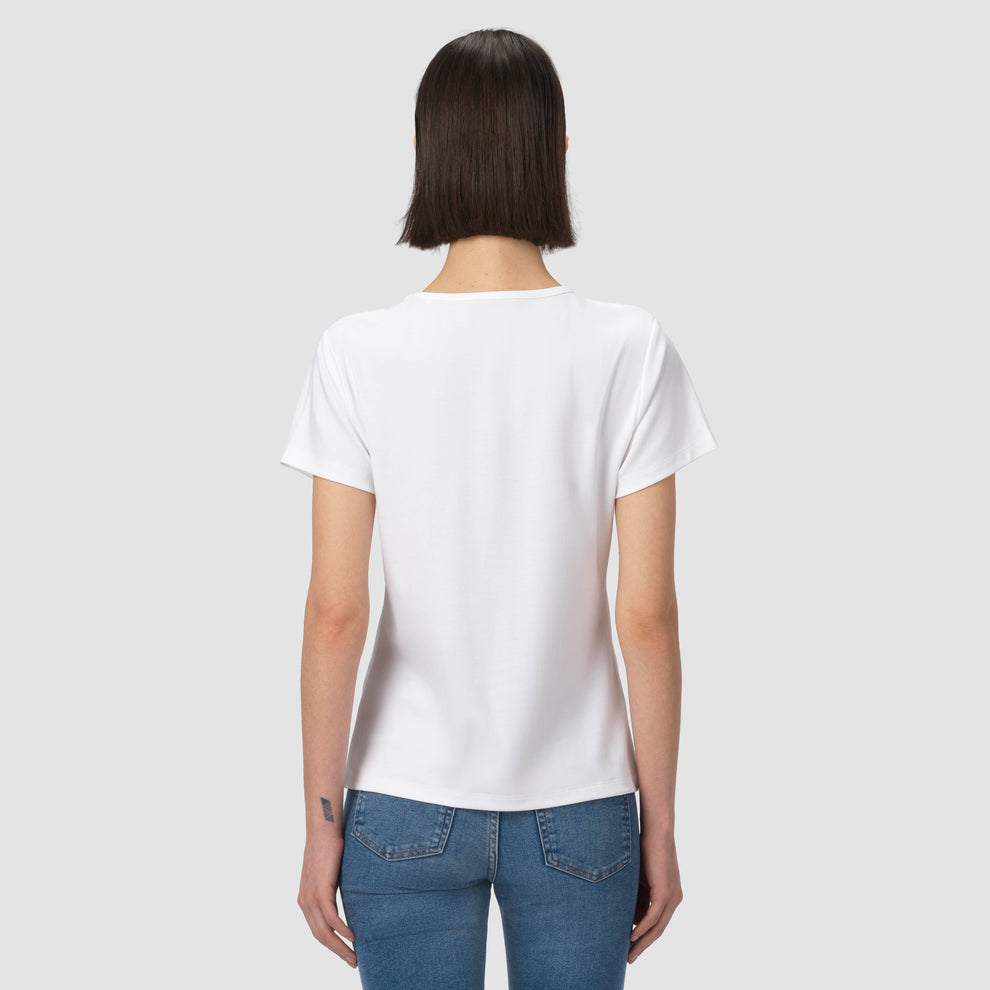 Une personne vêtue d'un t-shirt blanc uni et d'un jean bleu sur un fond gris clair