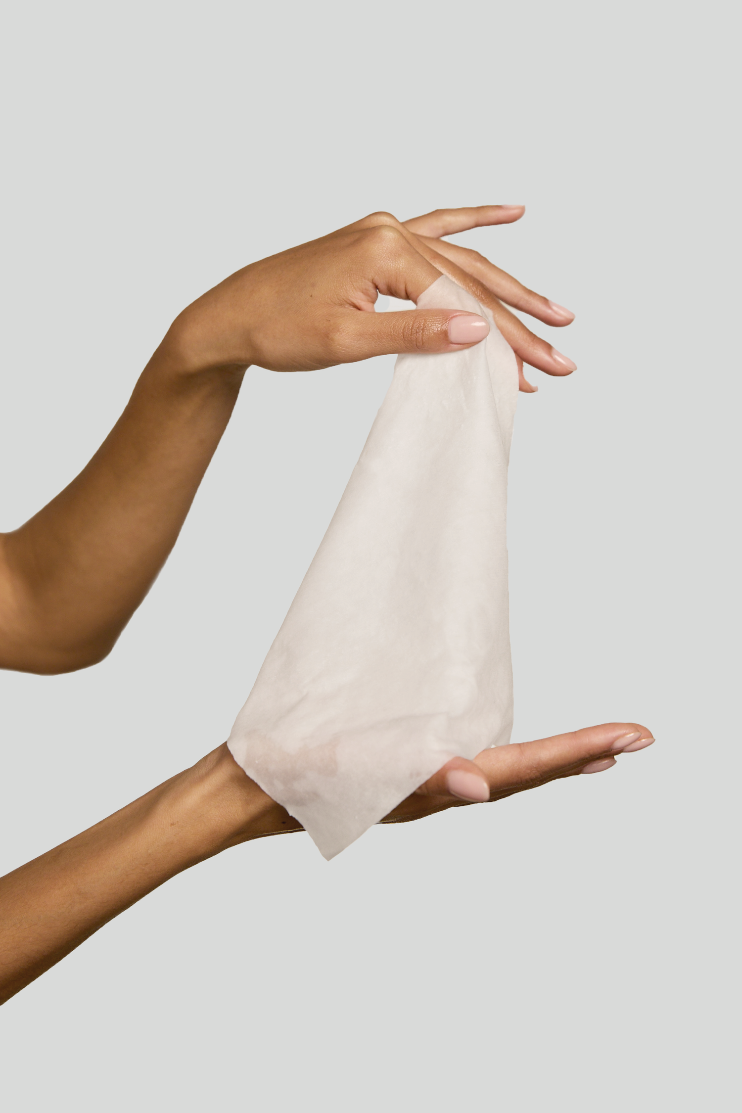 Main tenant une lingette en coton blanc humide sur un fond uni