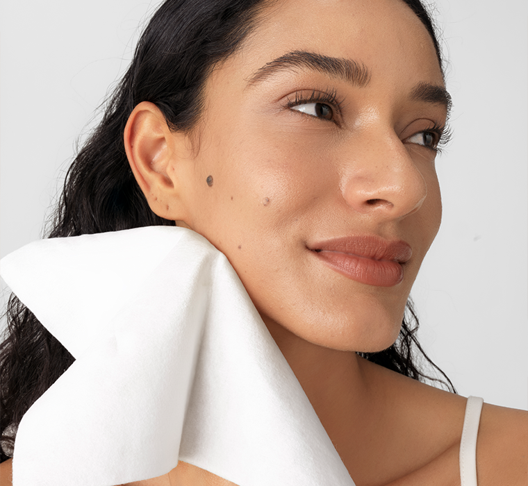 Woman with a white cotton towel cleaning her neck against a plain background