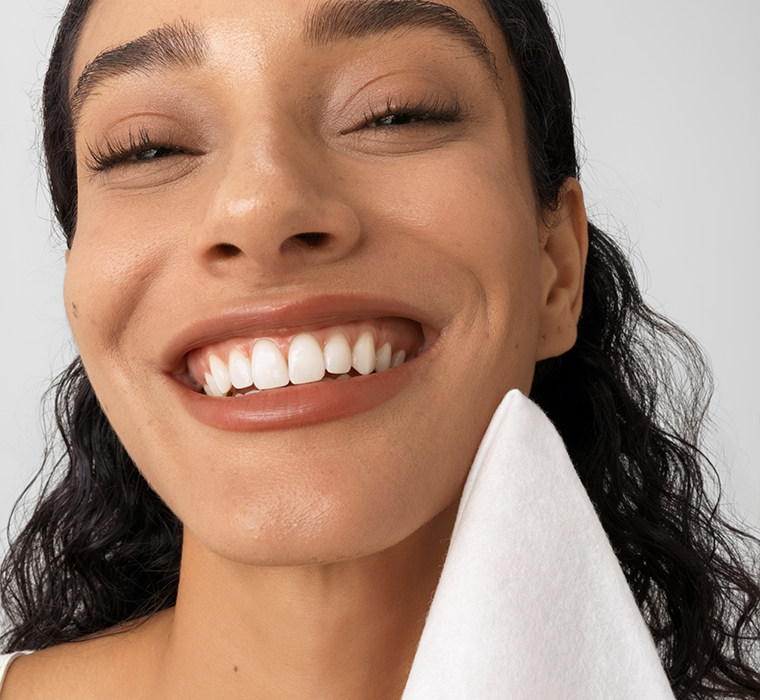Close-up of a woman with a bright smile holding cotton towelette against a neutral background