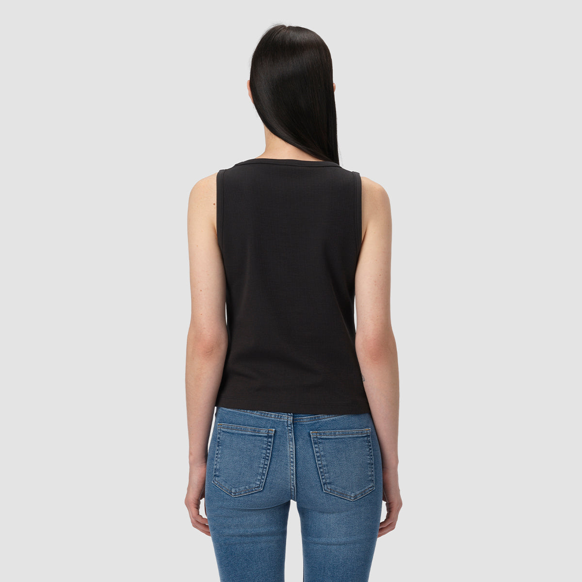 Person wearing a black tank top and blue jeans on a light gray background