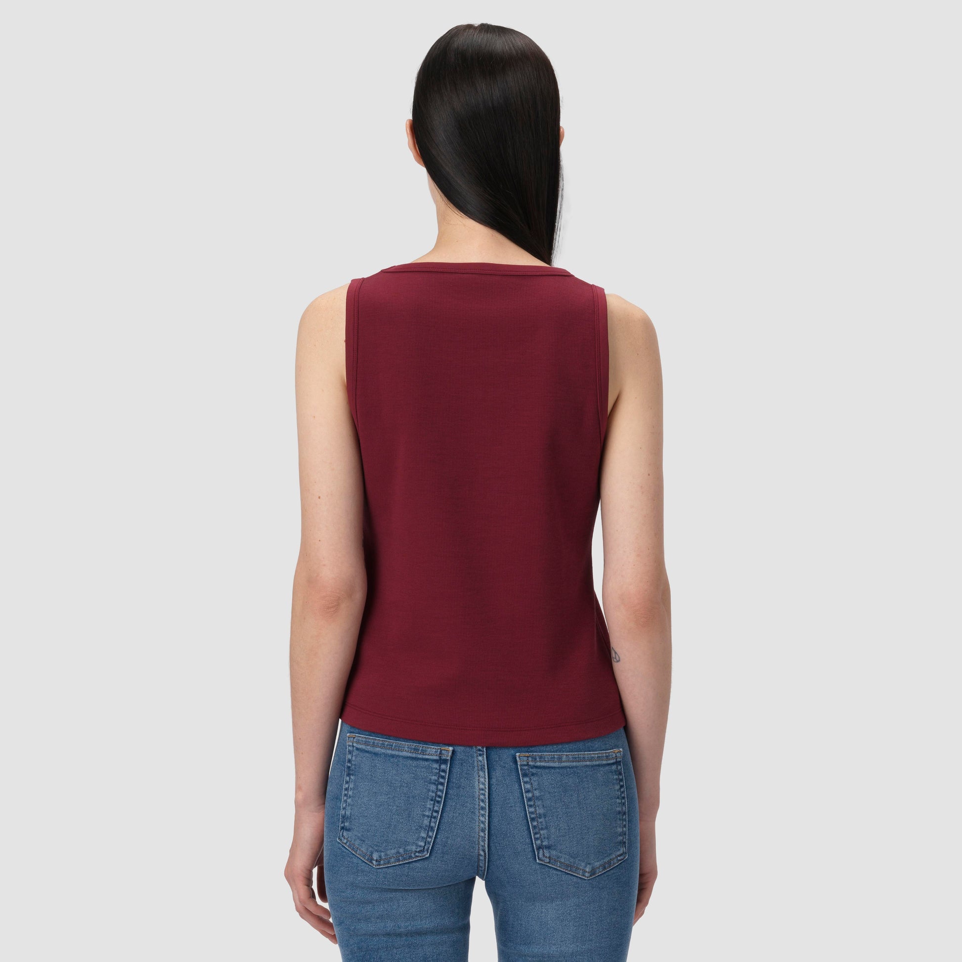 Person wearing a burgundy tank top and blue jeans on a light gray background