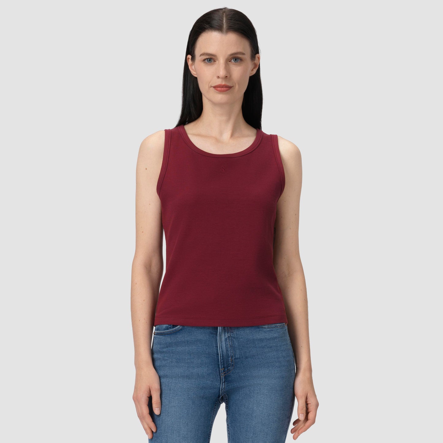 Woman wearing a burgundy tank top and blue jeans on a gray background