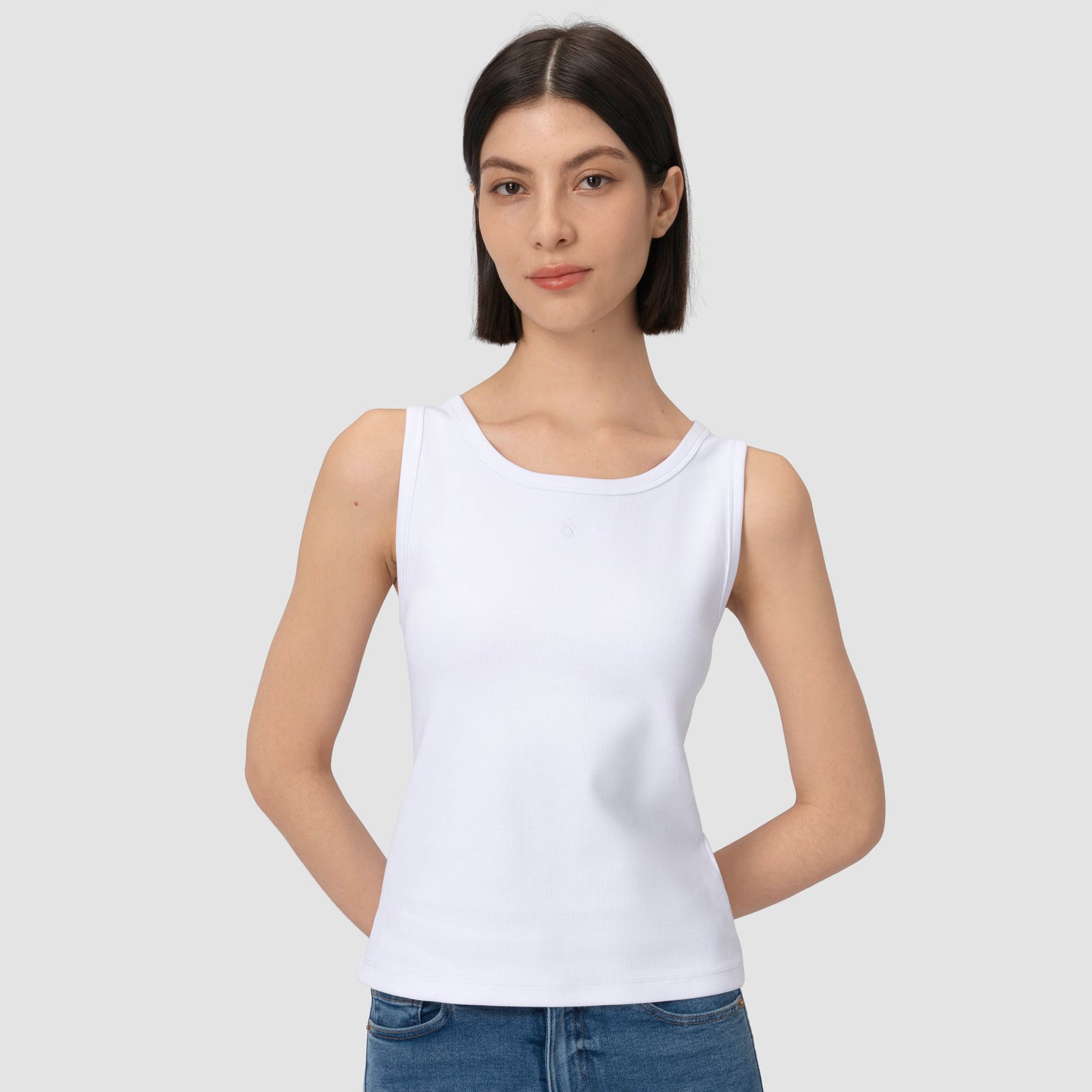 Model wearing white tank top against plain background