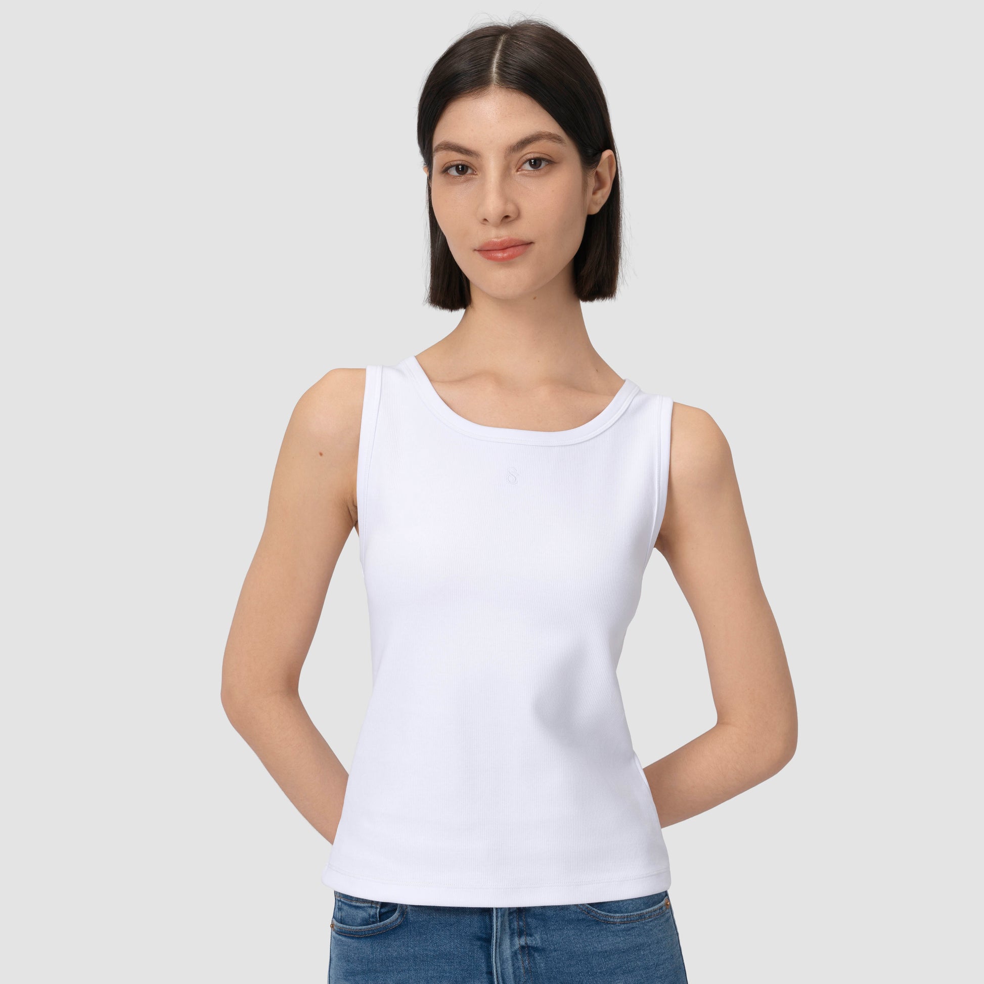 Model wearing white tank top against plain background