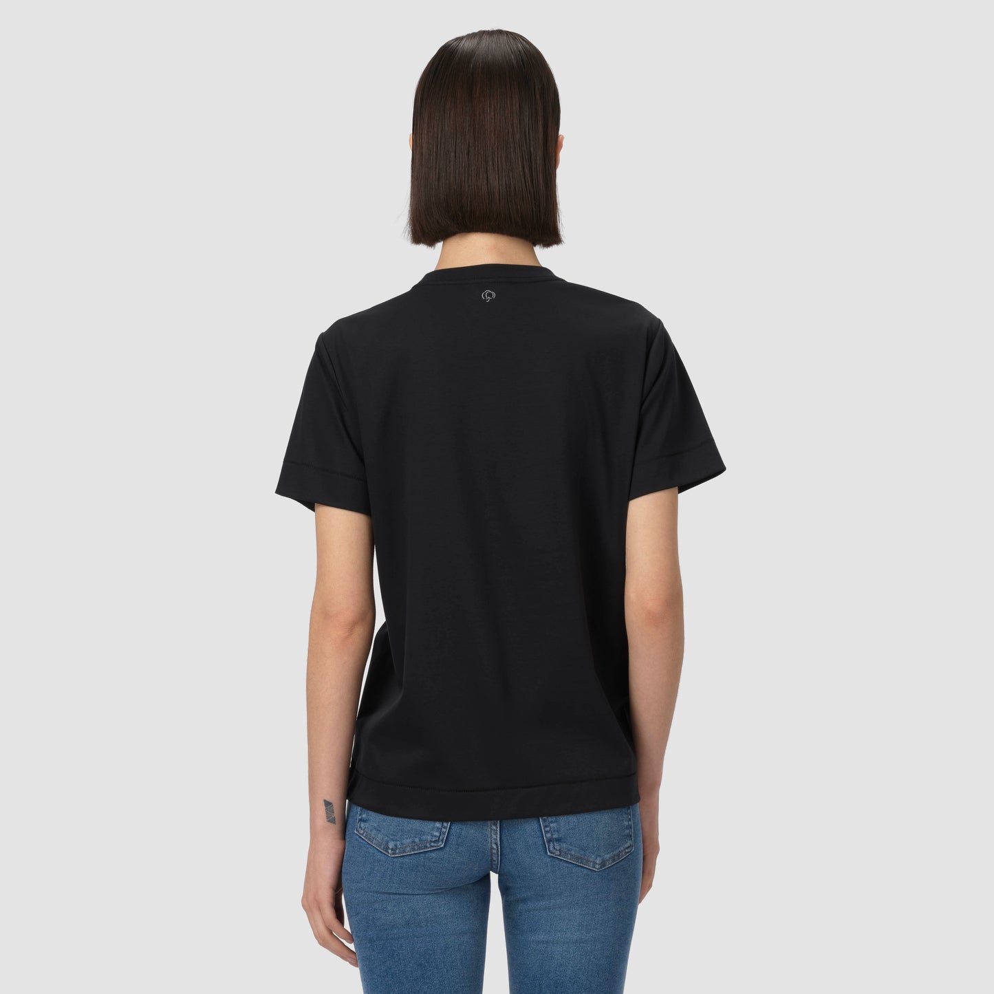 Person wearing a black t-shirt and blue jeans on a light gray background