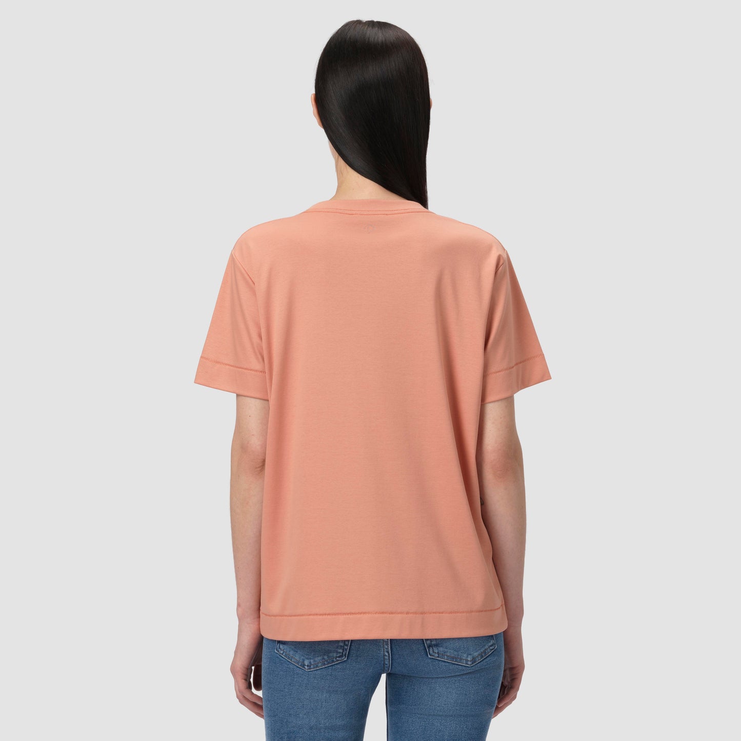 Person wearing a peach-colored t-shirt and blue jeans on a light gray background