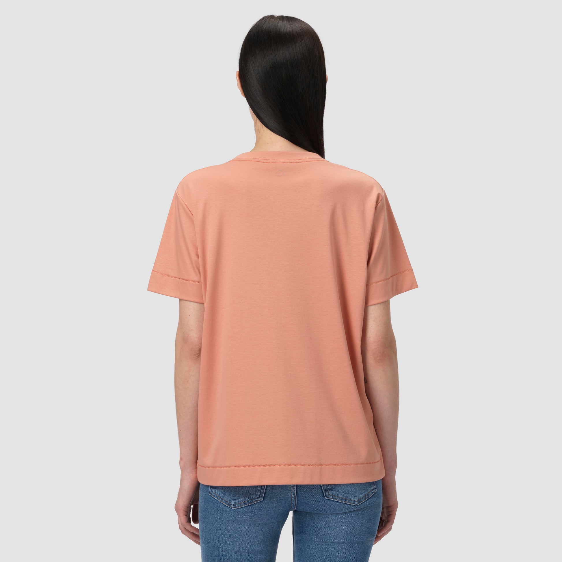 Person wearing a peach-colored t-shirt and blue jeans on a light gray background