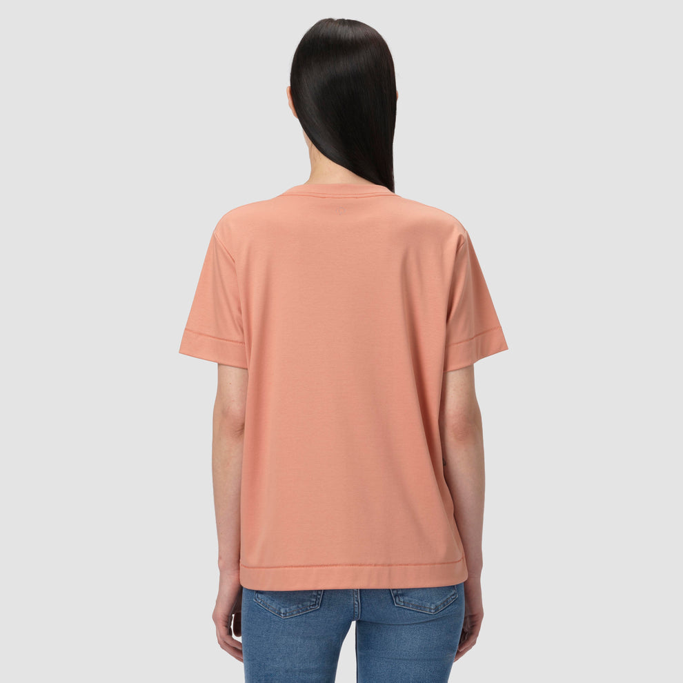 Une personne vêtue d'un t-shirt couleur pêche et d'un jean bleu sur un fond gris clair