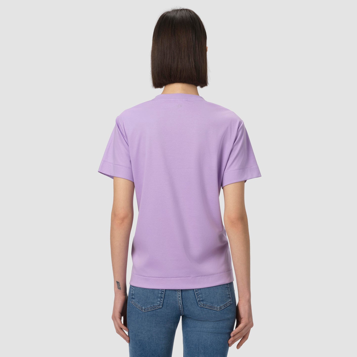 Person wearing a light purple t-shirt and blue jeans on a plain background