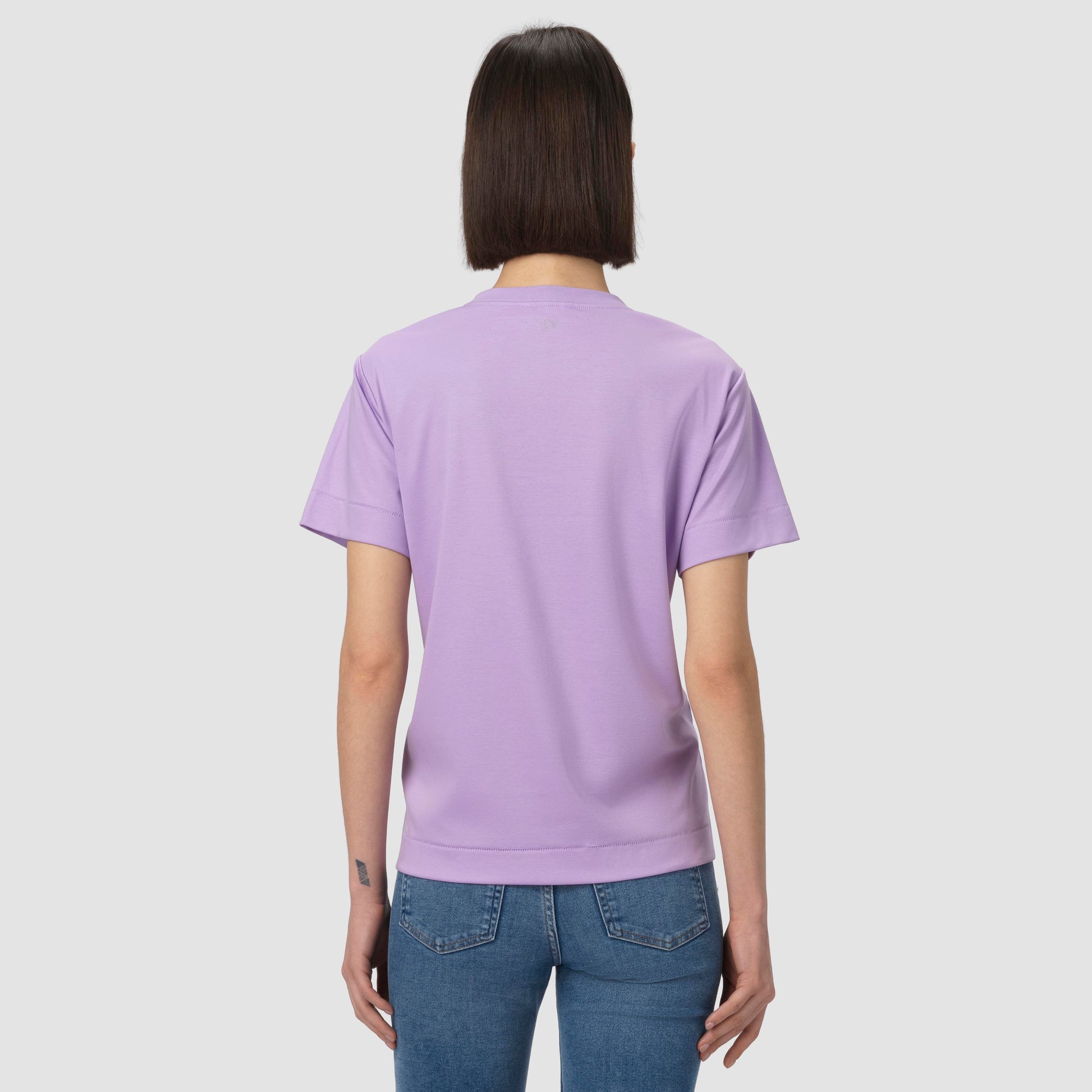 Person wearing a light purple t-shirt and blue jeans on a plain background