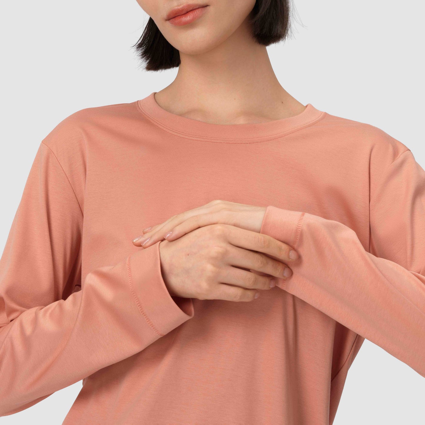 Gros plan sur un haut à manches longues dans des tons rose orangé, sur un fond uni gris