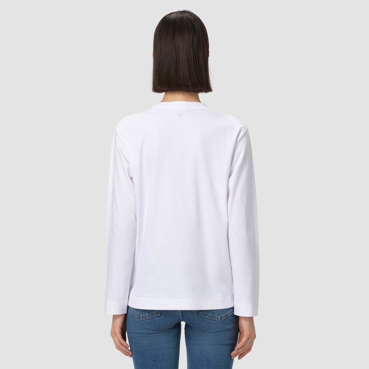 Une personne vêtue d'une chemise blanche à manches longues et d'un jean bleu sur un fond gris clair