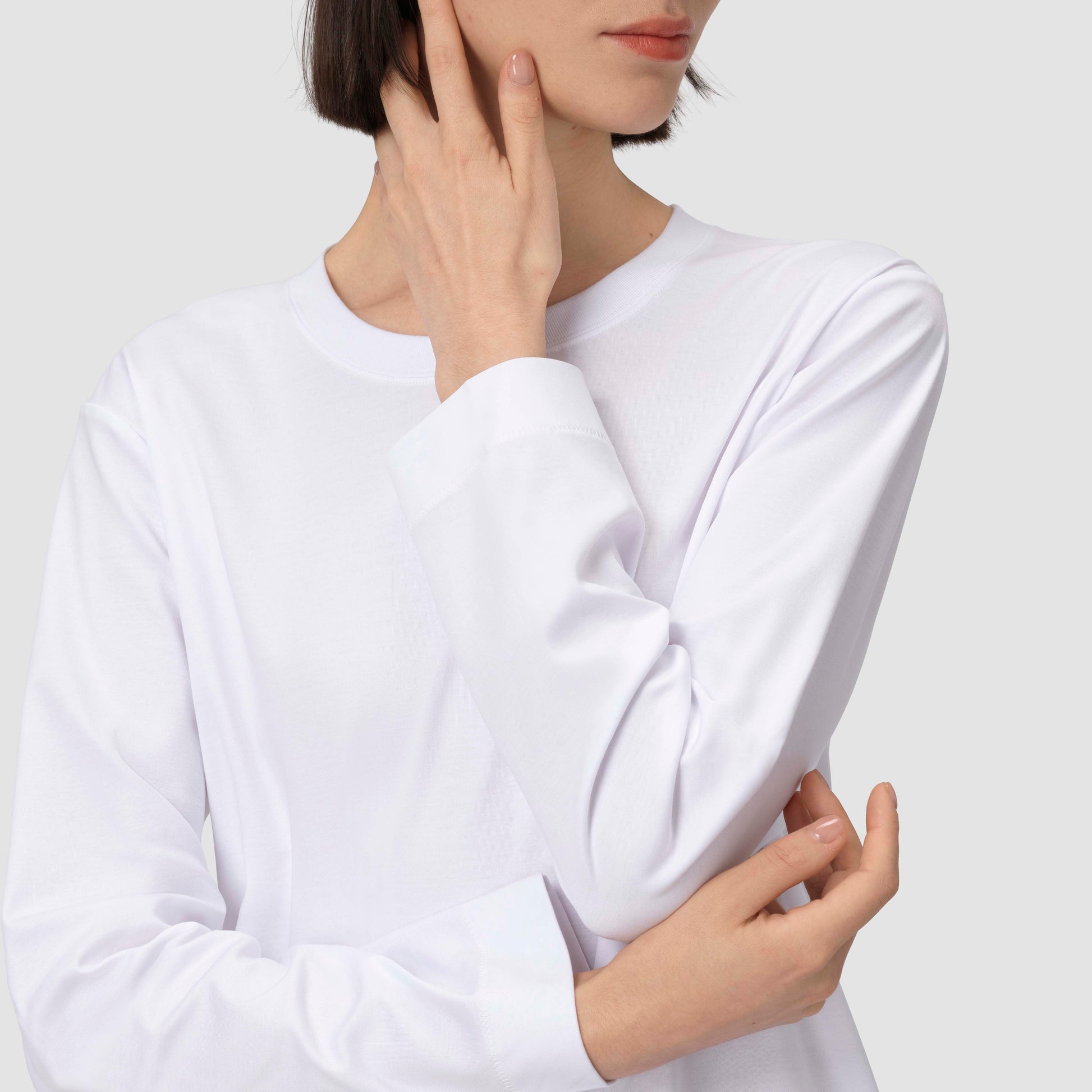 Une personne vêtue d'une chemise blanche à manches longues devant un fond uni