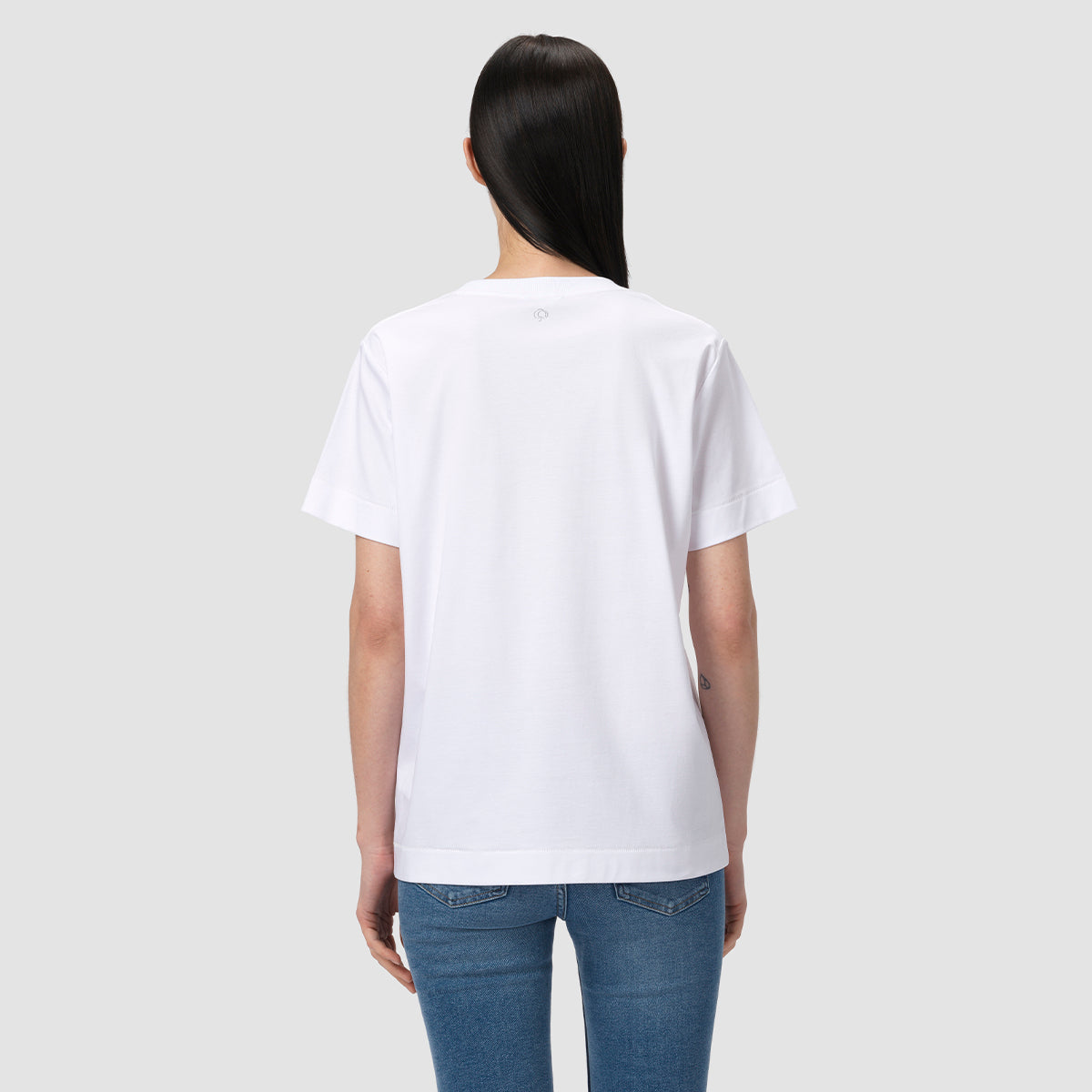 Person wearing a plain white t-shirt and blue jeans on a light gray background